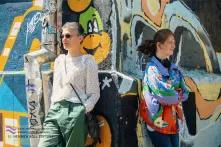 ესმა და ელენე დგანან გრაფიტით მოხატულ კედელთან და სხვადასხვა მხარეს იხედებიან